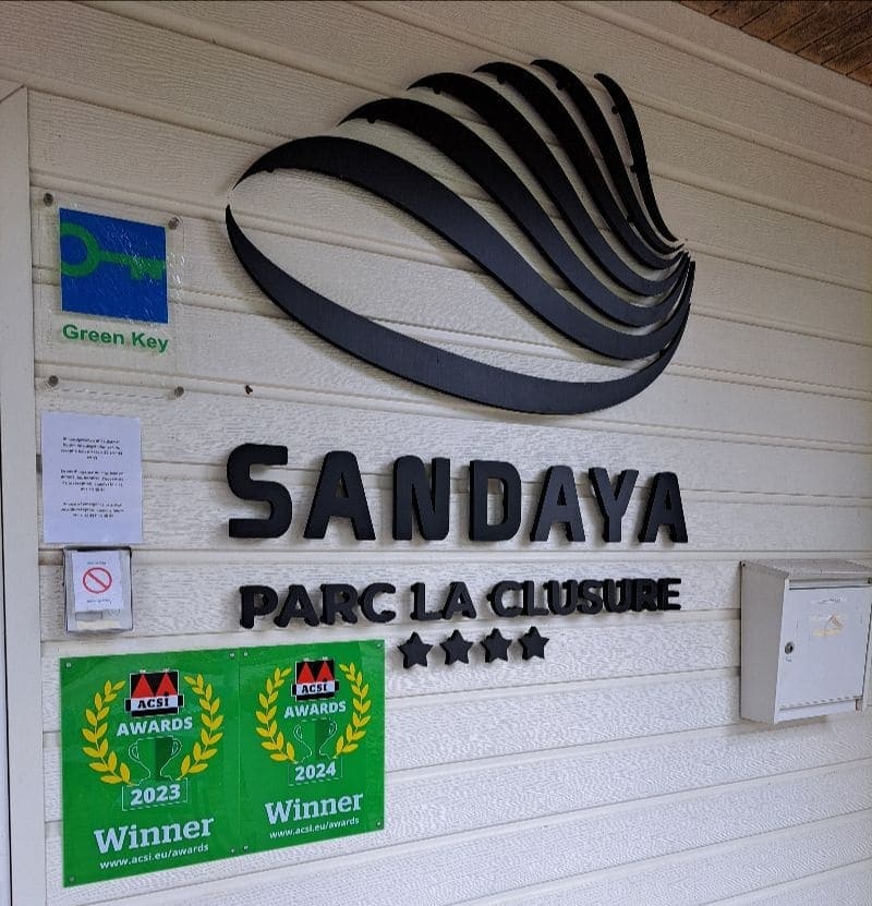 Entreebord van Sandaya Parc La Clusure in de Belgische Ardennen met het campinga-logo, vier sterren, Green Key-keurmerk en ACSI Awards voor 2023 en 2024.